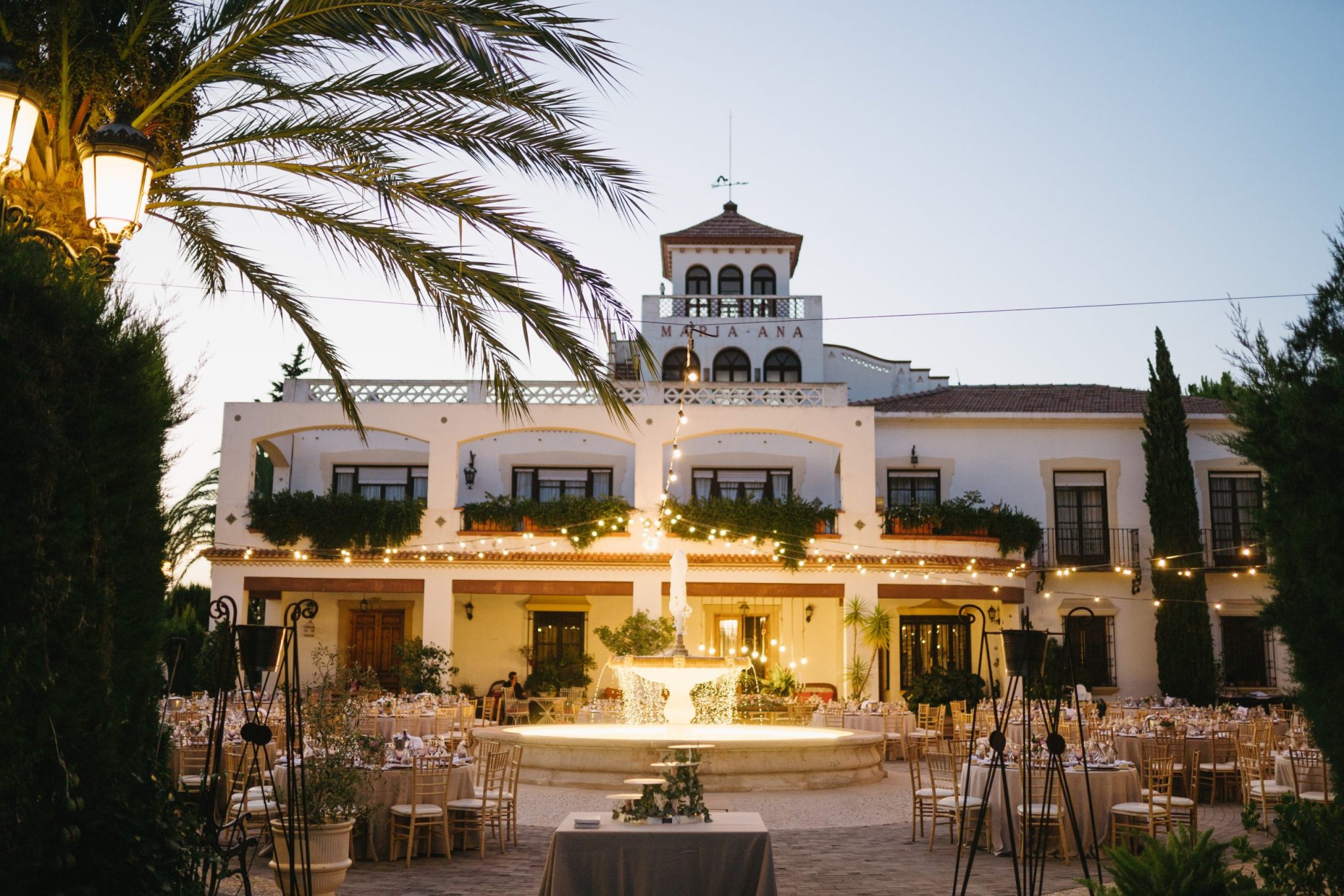 Caserón de Finca María Ana iluminado al anochecer, con la fuente encendida en el patio